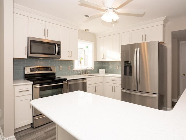 kitchen featuring decorative backsplash, appliances with stainless steel finishes, sink, white cabinetry, and hanging light fixtures