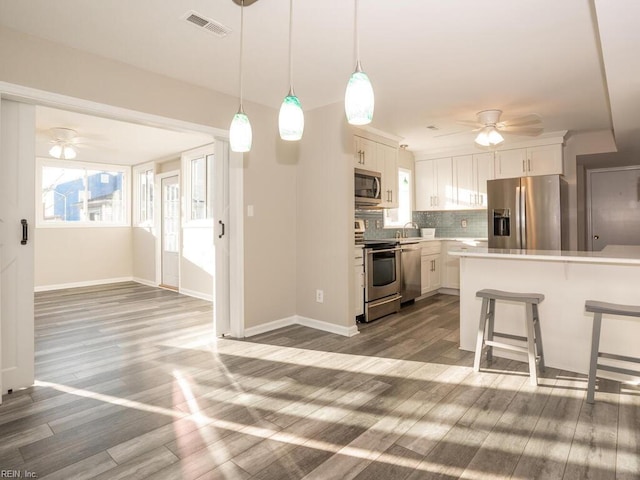 kitchen featuring decorative backsplash, dark hardwood / wood-style flooring, stainless steel appliances, decorative light fixtures, and white cabinets