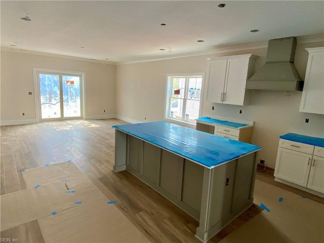 kitchen with white cabinetry, baseboards, light wood-style floors, ornamental molding, and custom range hood