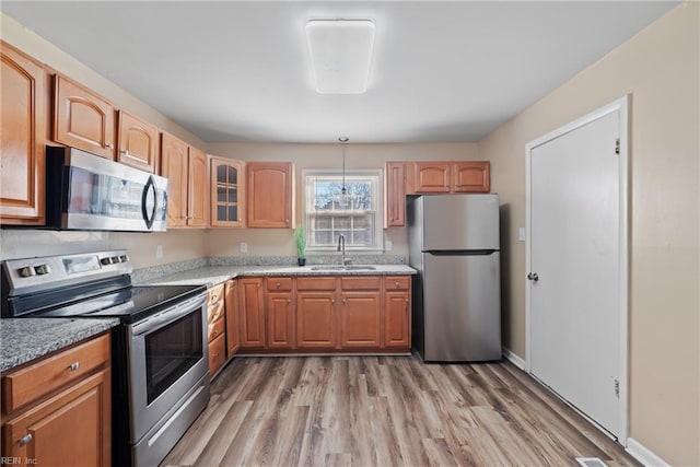 kitchen with light stone countertops, pendant lighting, light wood-type flooring, appliances with stainless steel finishes, and sink