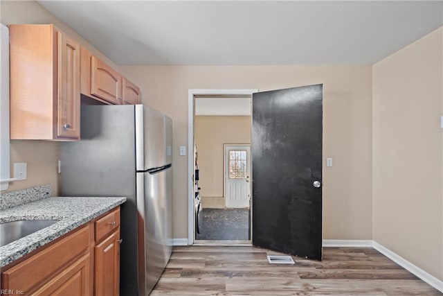 kitchen with stainless steel refrigerator, light brown cabinetry, light stone counters, sink, and light hardwood / wood-style flooring