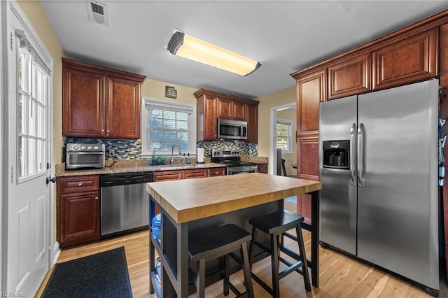 kitchen with sink, light wood-type flooring, stainless steel appliances, and tasteful backsplash