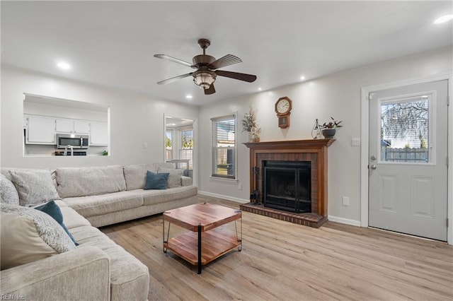 living room featuring ceiling fan, light hardwood / wood-style floors, a healthy amount of sunlight, and a fireplace