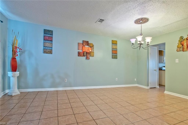 tiled empty room featuring a textured ceiling and a notable chandelier