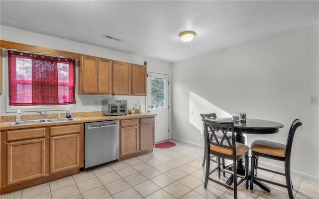 kitchen featuring stainless steel dishwasher, light tile patterned floors, sink, and a textured ceiling