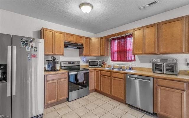 kitchen featuring light tile patterned flooring, a textured ceiling, stainless steel appliances, and sink