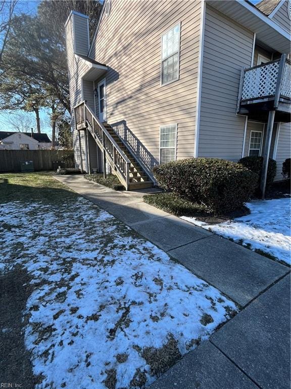 view of snow covered exterior featuring fence, a chimney, a balcony, and stairs