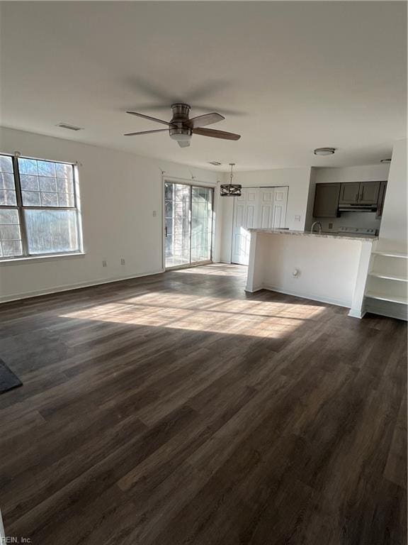 unfurnished living room featuring ceiling fan, a healthy amount of sunlight, and dark hardwood / wood-style floors