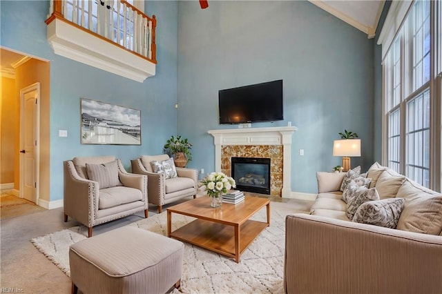 living room featuring a towering ceiling, a tiled fireplace, ornamental molding, and a healthy amount of sunlight