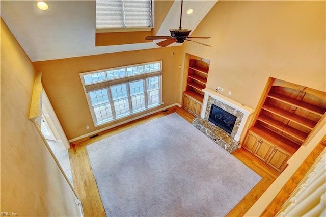 unfurnished living room featuring a towering ceiling, a fireplace, ceiling fan, and wood-type flooring