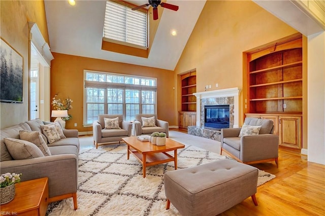 living room featuring a towering ceiling, ceiling fan, a fireplace, light hardwood / wood-style flooring, and built in features