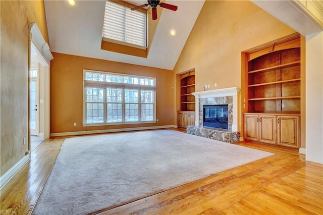 unfurnished living room featuring ceiling fan, light hardwood / wood-style flooring, built in features, and a towering ceiling