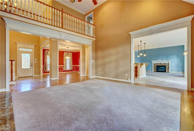 unfurnished living room with a high ceiling, ceiling fan, crown molding, and a stone fireplace