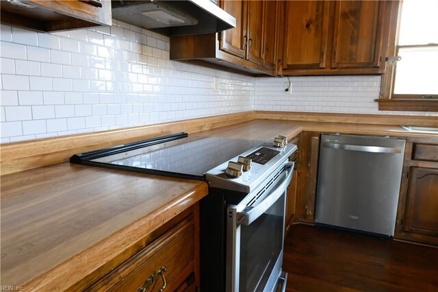 kitchen featuring wood counters, stainless steel appliances, extractor fan, and tasteful backsplash