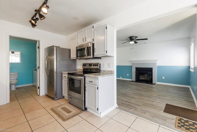 kitchen with light tile patterned flooring, a fireplace, white cabinets, ceiling fan, and stainless steel appliances