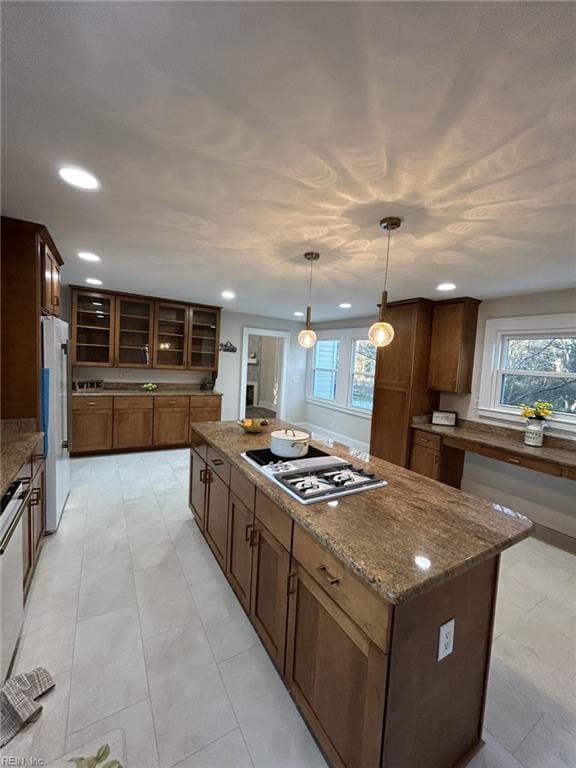 kitchen featuring a kitchen island, dark stone counters, white fridge, hanging light fixtures, and stainless steel gas stovetop