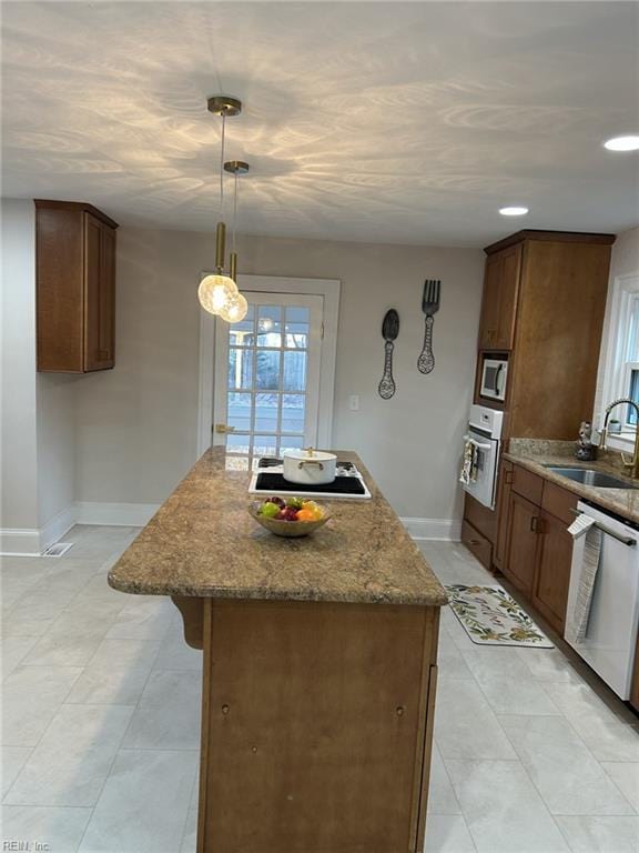 kitchen with a center island, white appliances, light stone countertops, hanging light fixtures, and sink