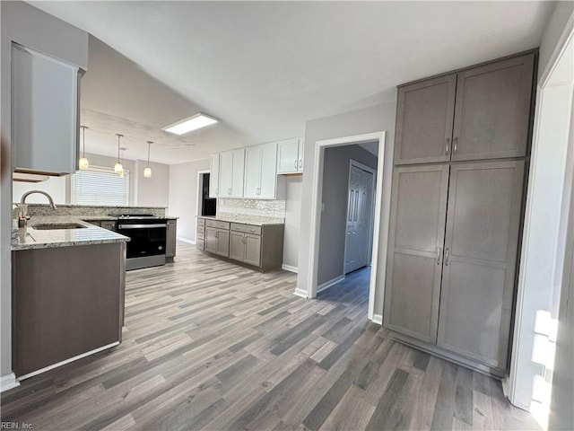 kitchen featuring dark hardwood / wood-style floors, sink, stainless steel range with electric cooktop, decorative light fixtures, and backsplash