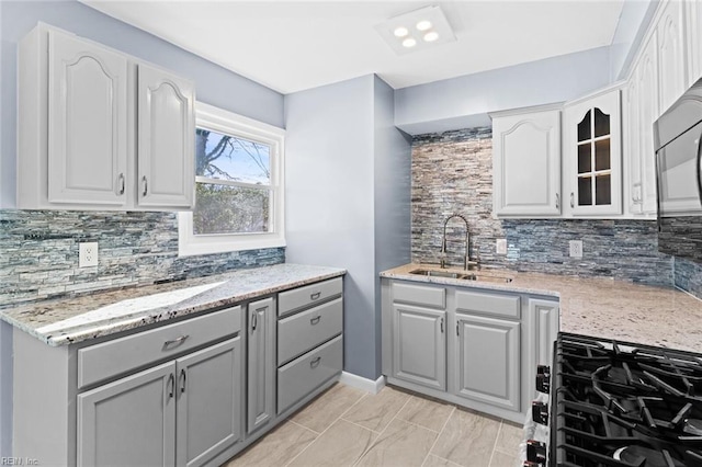 kitchen featuring light stone countertops, gray cabinetry, backsplash, and sink