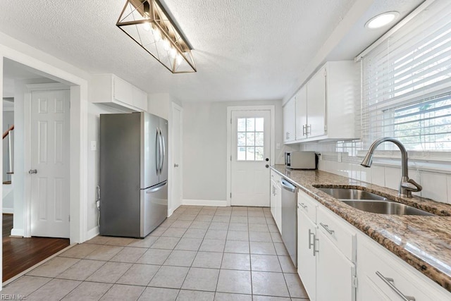 kitchen with appliances with stainless steel finishes, sink, light tile patterned floors, dark stone countertops, and white cabinets