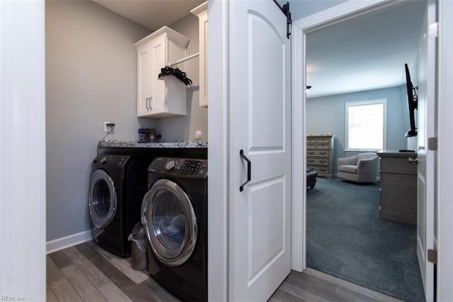 washroom featuring washing machine and clothes dryer, a barn door, cabinets, and wood-type flooring