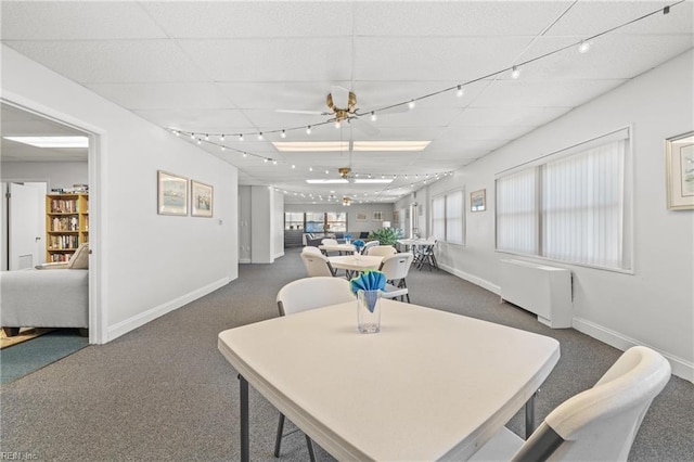 dining room with ceiling fan, a drop ceiling, dark carpet, and radiator