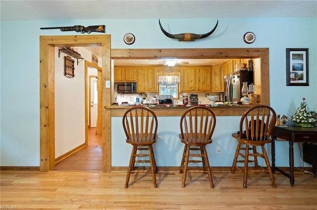 kitchen featuring light hardwood / wood-style flooring, ceiling fan, a kitchen bar, kitchen peninsula, and stainless steel refrigerator