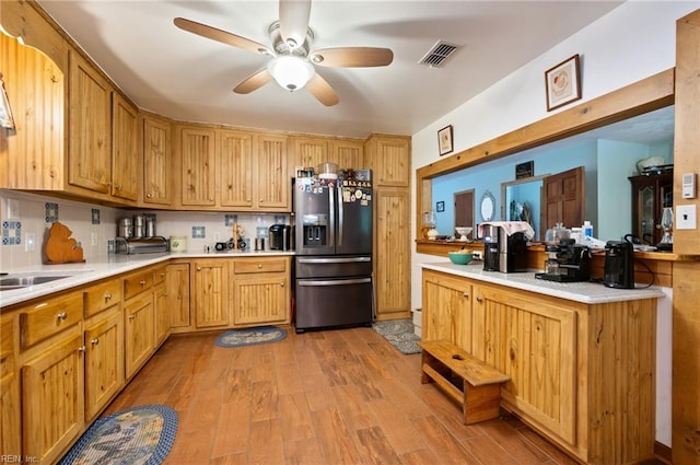 kitchen with decorative backsplash, stainless steel refrigerator with ice dispenser, light wood-type flooring, ceiling fan, and sink