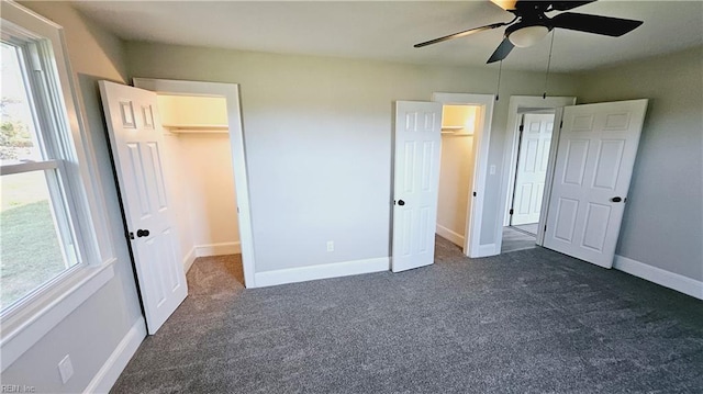 unfurnished bedroom featuring ceiling fan, a closet, a spacious closet, and dark colored carpet