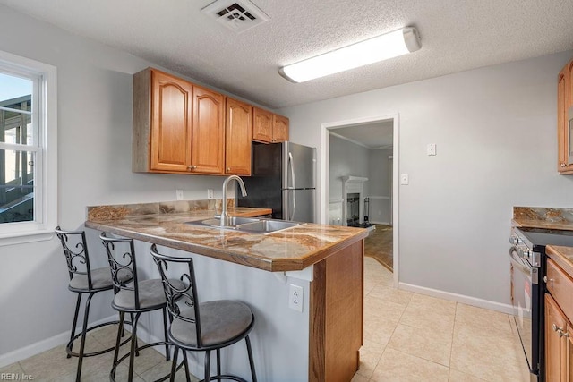 kitchen featuring stainless steel appliances, kitchen peninsula, a textured ceiling, a breakfast bar, and sink