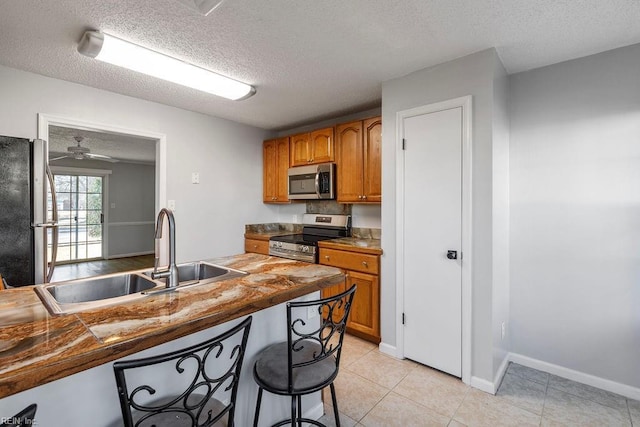 kitchen featuring stainless steel appliances, sink, a textured ceiling, ceiling fan, and a breakfast bar area