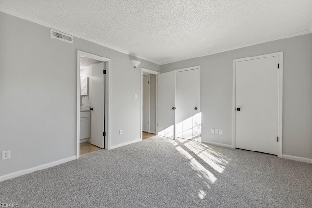 unfurnished bedroom featuring ensuite bathroom, light colored carpet, ornamental molding, and a textured ceiling