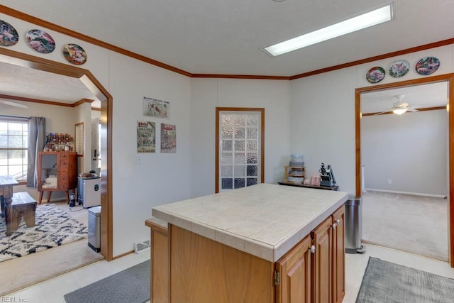 kitchen featuring crown molding, ceiling fan, tile counters, and a center island