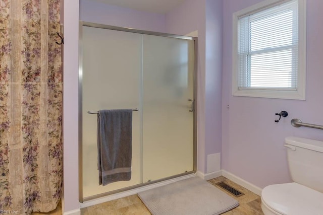 bathroom featuring toilet, a shower with door, and plenty of natural light