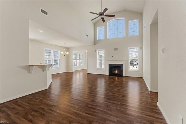 unfurnished living room with dark hardwood / wood-style flooring, a towering ceiling, and ceiling fan with notable chandelier