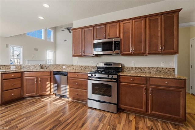 kitchen with light stone countertops, appliances with stainless steel finishes, ceiling fan, and hardwood / wood-style flooring