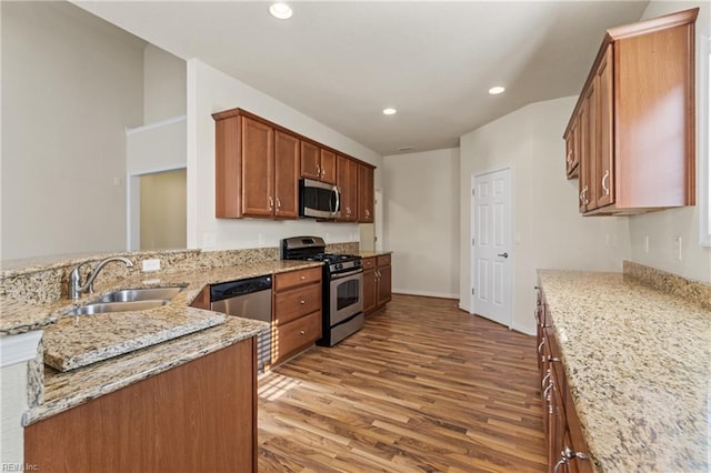 kitchen with sink, light stone counters, light wood-type flooring, kitchen peninsula, and appliances with stainless steel finishes