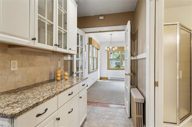 interior space featuring decorative light fixtures, white cabinetry, an inviting chandelier, tasteful backsplash, and light stone countertops