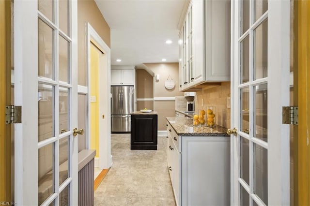 kitchen with white cabinets, backsplash, dark stone counters, and stainless steel fridge