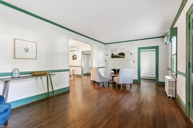 living room featuring a wall unit AC, crown molding, radiator, dark wood-type flooring, and a brick fireplace