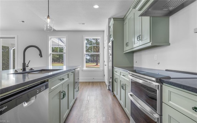 kitchen with hardwood / wood-style flooring, pendant lighting, custom range hood, appliances with stainless steel finishes, and sink