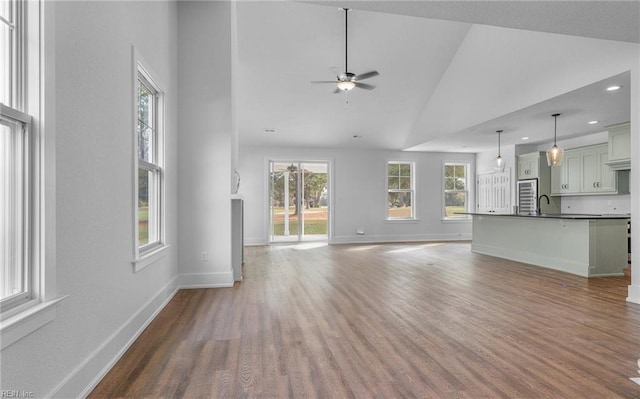 unfurnished living room with sink, high vaulted ceiling, ceiling fan, and a healthy amount of sunlight