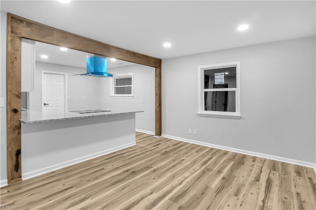 kitchen with light wood-type flooring, white cabinetry, island range hood, and light stone countertops