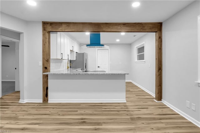 kitchen featuring light stone counters, white cabinets, light hardwood / wood-style flooring, and island range hood