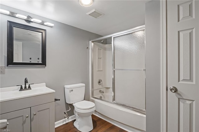 full bathroom with hardwood / wood-style floors, combined bath / shower with glass door, vanity, and toilet