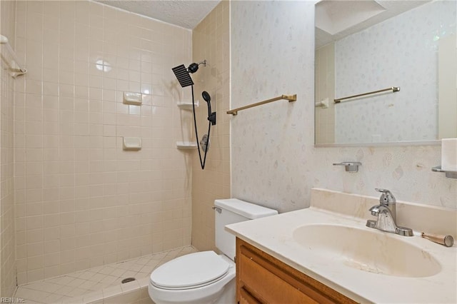 bathroom featuring a textured ceiling, toilet, tiled shower, and vanity