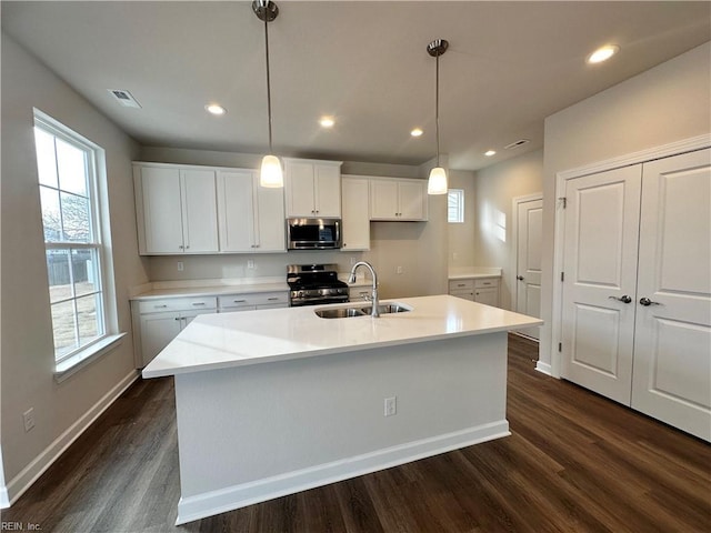 kitchen featuring pendant lighting, stainless steel appliances, a center island with sink, white cabinetry, and sink