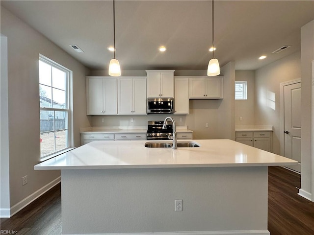 kitchen with an island with sink, appliances with stainless steel finishes, and hanging light fixtures