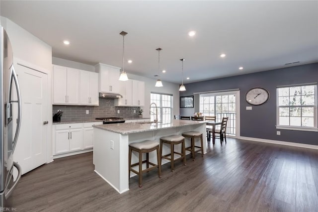 kitchen with decorative light fixtures, white cabinets, an island with sink, and light stone counters