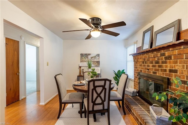 dining area with a brick fireplace, ceiling fan, and light hardwood / wood-style flooring